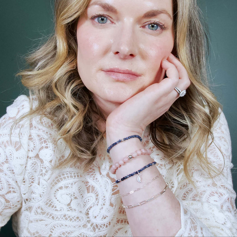 A close-up portrait of a woman wearing a bracelet stack of Pink Opal, Sapphire, and sterling silver.