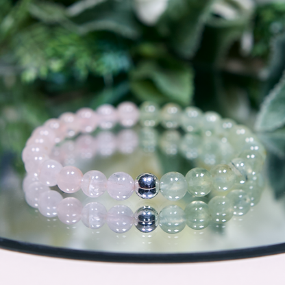Pale pink Madagascar Rose Quartz and pale green Prehnite beaded gemstone bracelet with smooth round beads and a sterling silver accent bead on a mirrored background