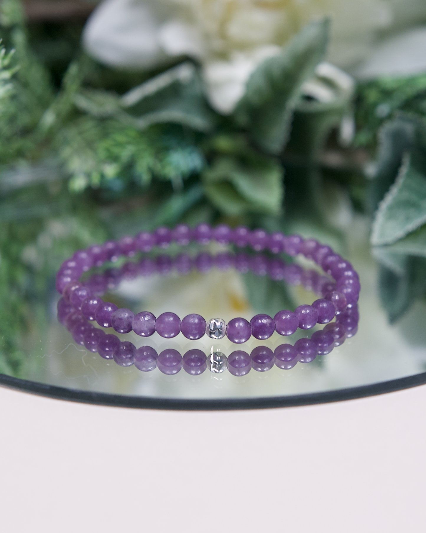 Purple Lepidolite beaded bracelet with a sterling silver accent bead on a reflective surface with green foliage in the background