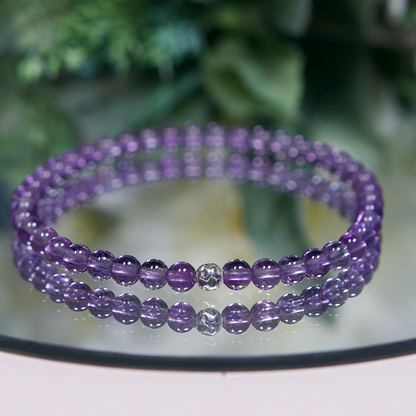 A medium-shade purple Amethyst beaded bracelet with smooth round high clarity beads and a hammered sterling silver accent bead on a mirrored plate