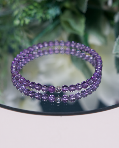 A medium-shade purple Amethyst beaded bracelet with smooth round high clarity beads and a hammered sterling silver accent bead on a mirrored plate
