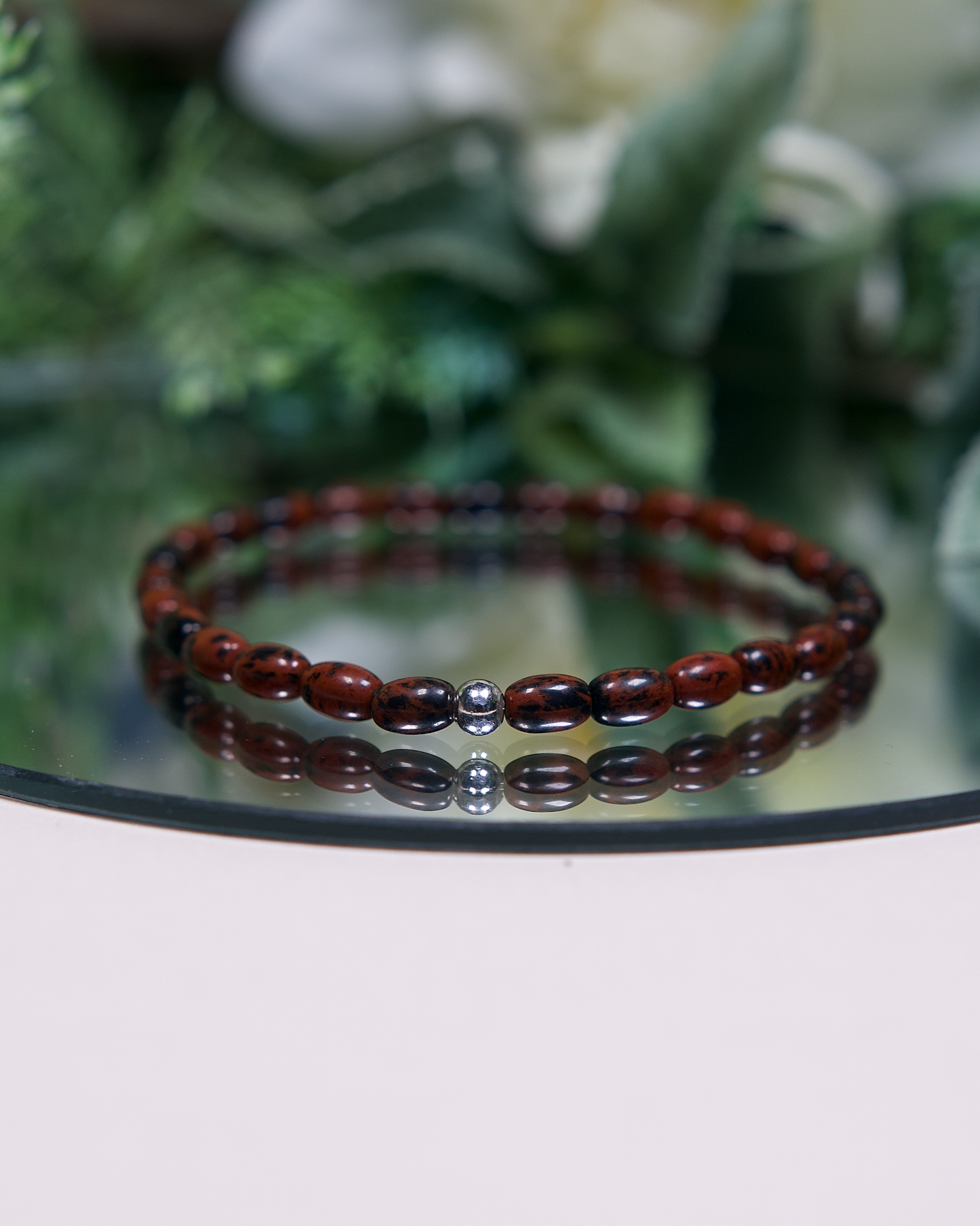 Close up photo of Mahogany Obsidian beaded bracelet with barrel-shaped beads and a sterling silver accent bead.