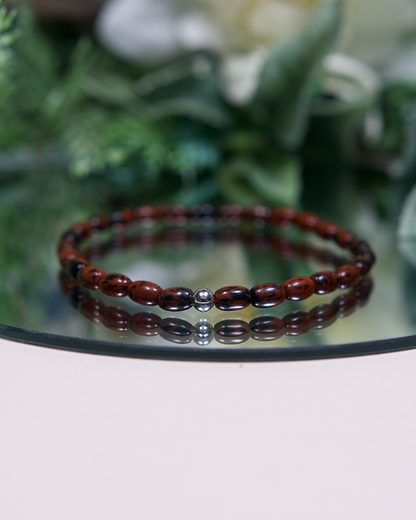 Reddish brown and black barrel-shaped Mahogany Obsidian beaded bracelet with a sterling silver accent bead on mirrored plate
