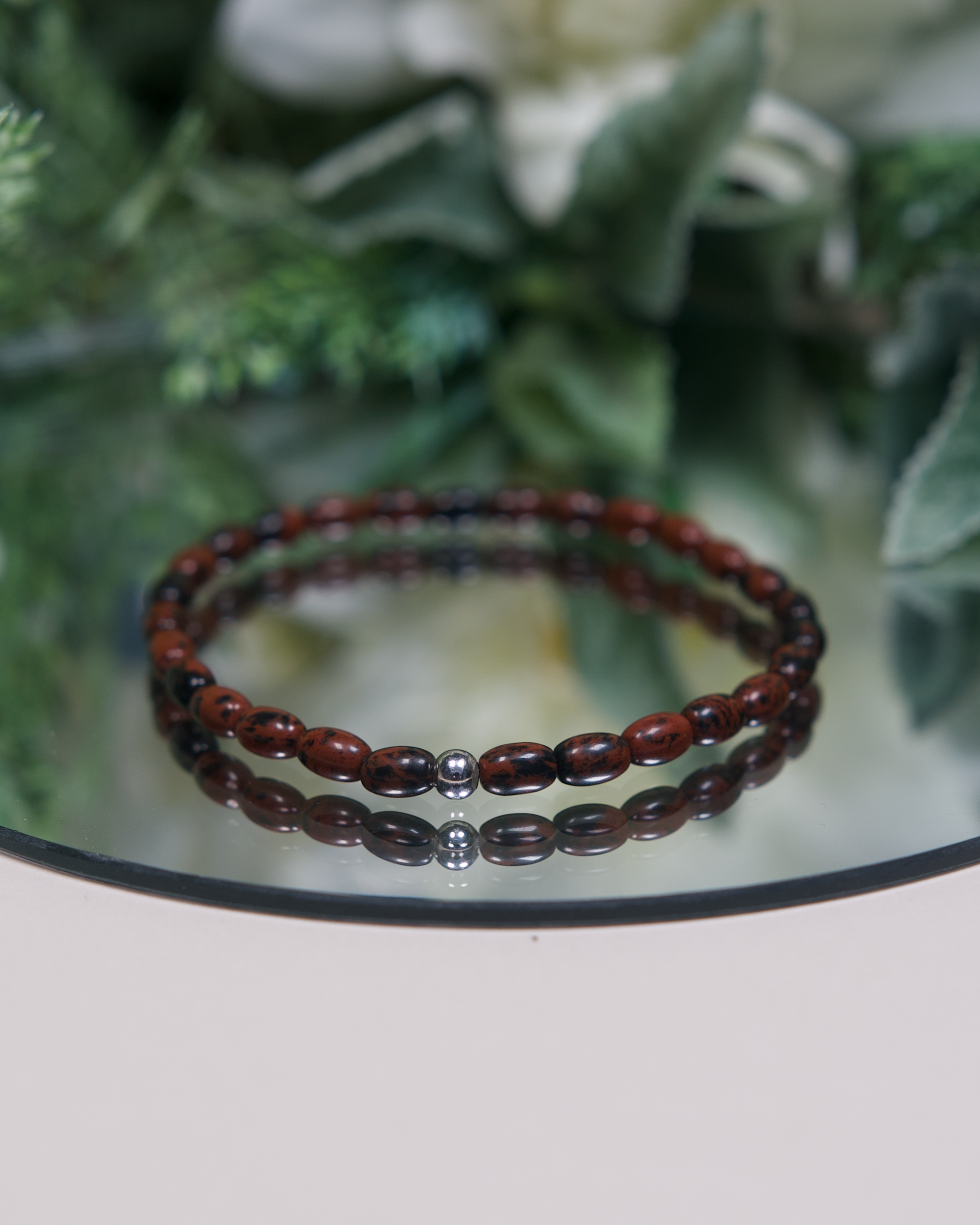 Close up photo of Mahogany Obsidian beaded bracelet with barrel-shaped beads and a sterling silver accent bead.