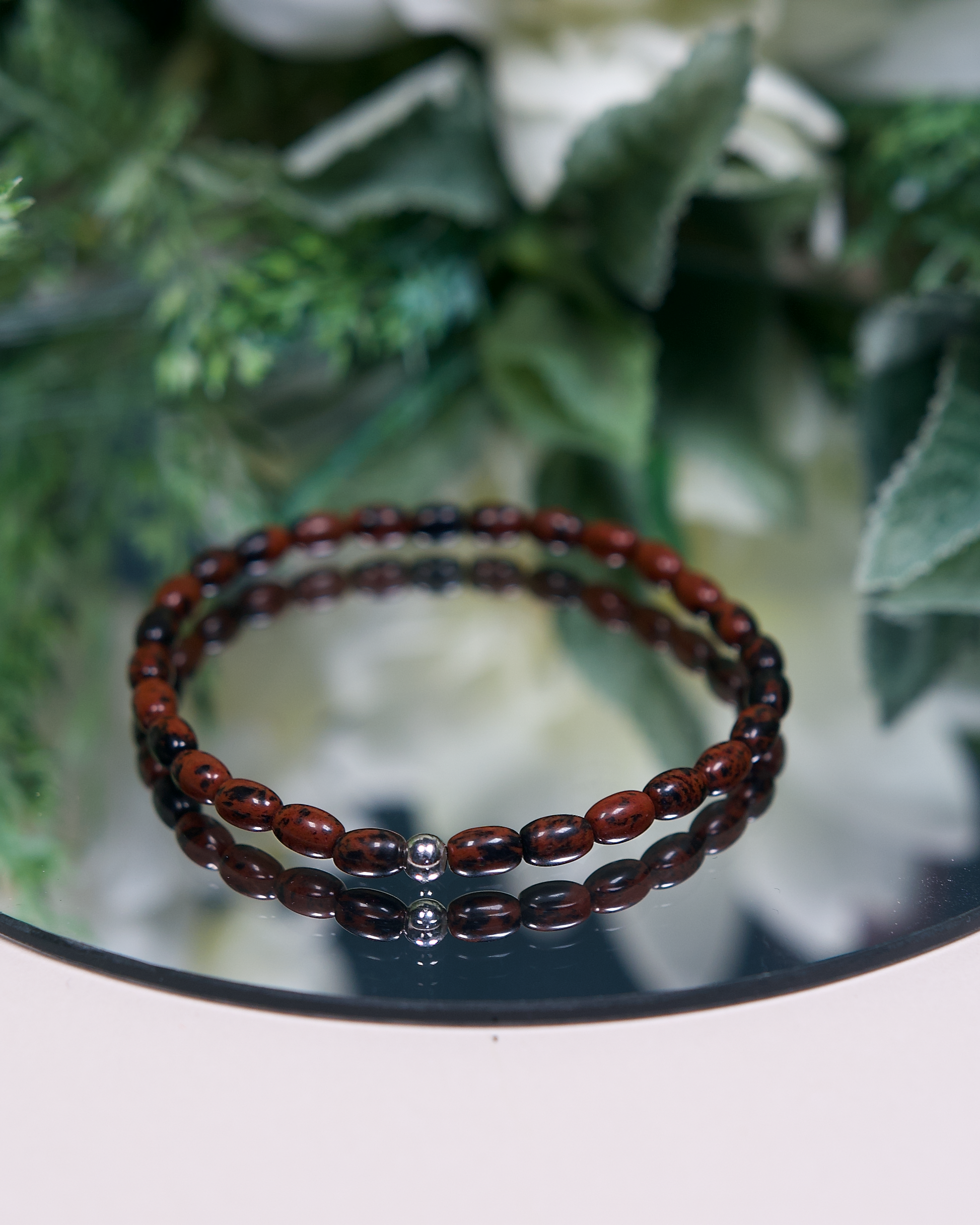 Close up photo of Mahogany Obsidian beaded bracelet with barrel-shaped beads and a sterling silver accent bead.