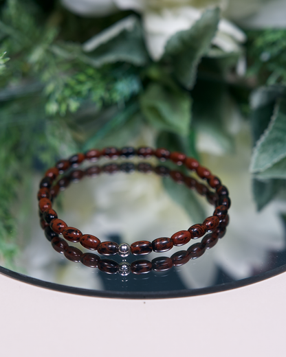 Reddish brown and black barrel-shaped Mahogany Obsidian beaded bracelet with a sterling silver accent bead on mirrored plate