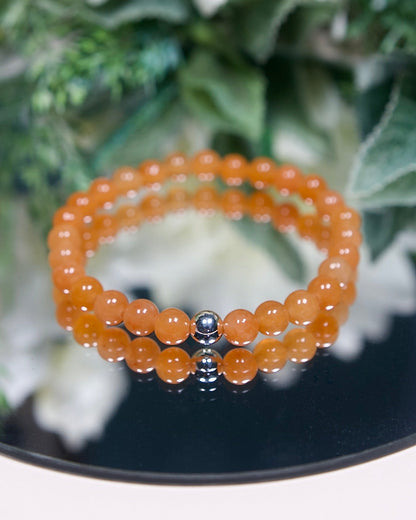 A Red Aventurine beaded gemstone bracelet with bright orange round smooth beads and a sterling silver accent bead on a mirrored plate