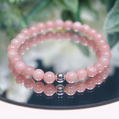 A pastel Pink Opal beaded gemstone bracelet with smooth round beads and a sterling silver accent bead on a mirrored background