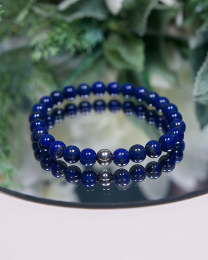 A deep rich blue Lapis Lazuli beaded gemstone bracelet with smooth round beads and a sterling silver accent bead on a mirrored plate