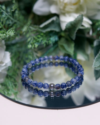 A Blue Spot Jasper beaded gemstone bracelet with mottled dark and pale blue beads and a sterling silver accent bead on a mirrored plate
