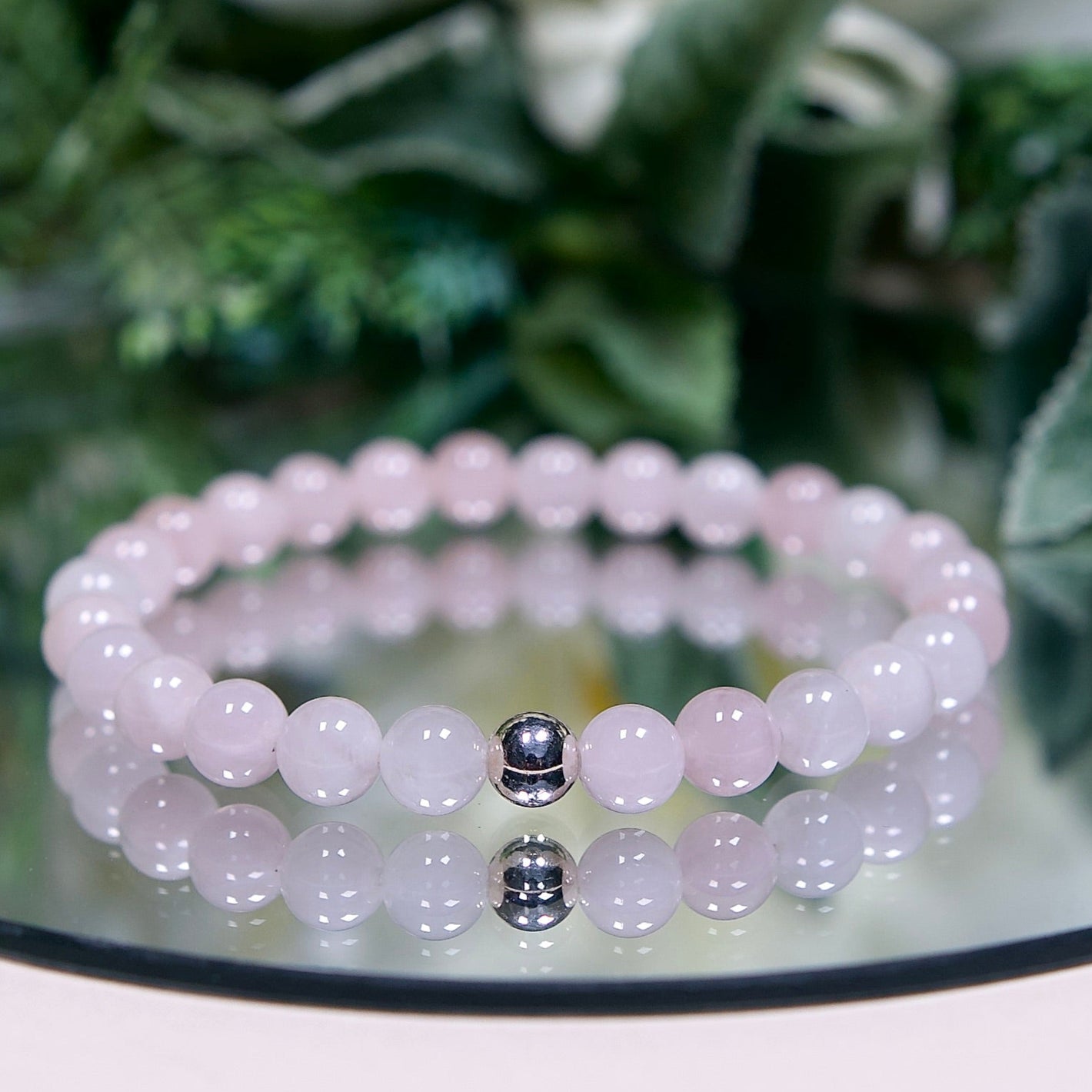 A pale opaque pink Madagascar Rose Quartz beaded gemstone bracelet with smooth round beads and a sterling silver accent bead on a mirrored plate