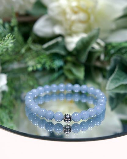 A powder blue beaded bracelet with smooth round Angelite gemstone beads and sterling silver accent bead on a mirrored plate