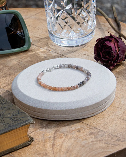 Peach and grey moonstone beaded gemstone bracelet with sterling silver spring ring clasp on coaster on wooden table