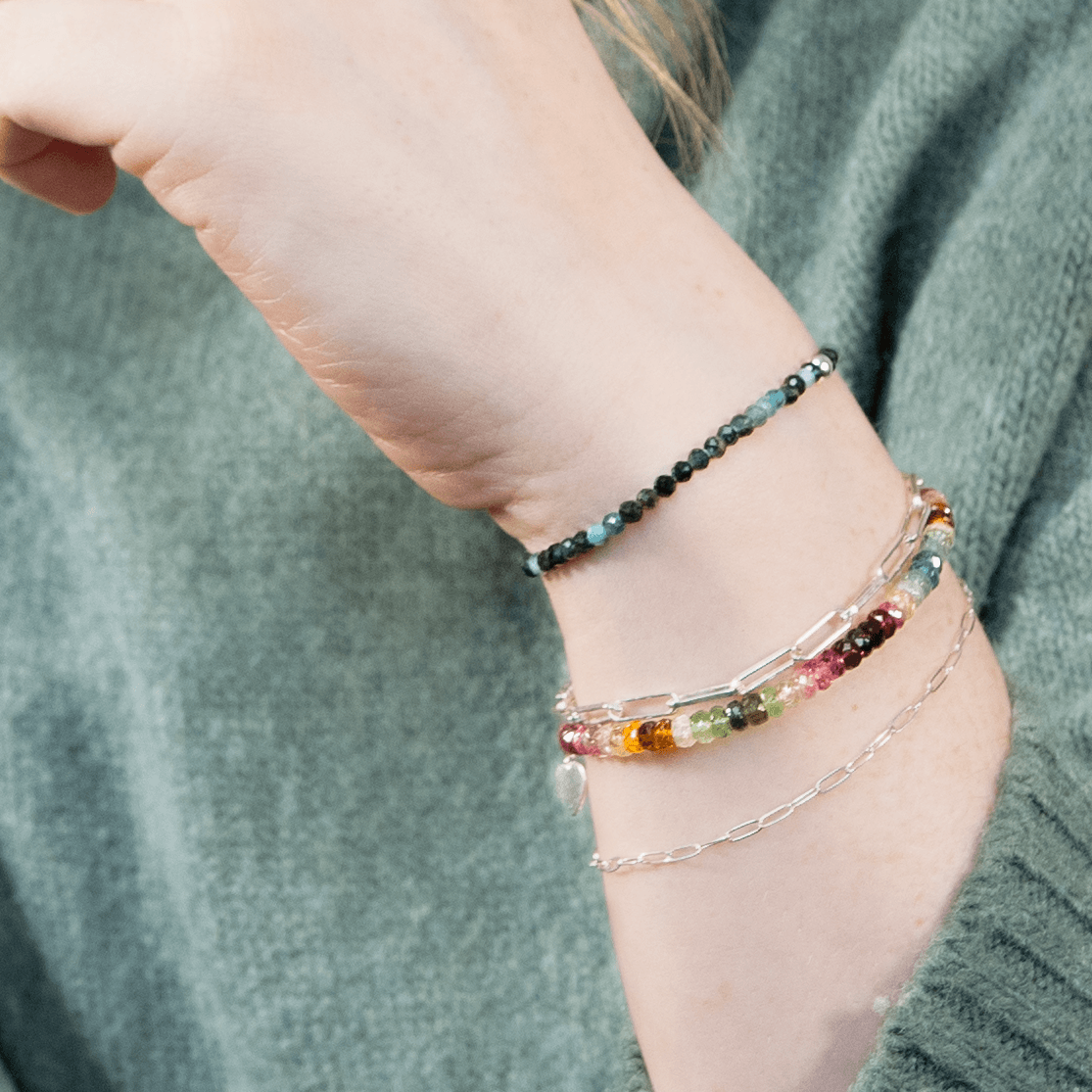 A closeup of a woman's wrist with a watermelon tourmaline bracelet with silver and blue bracelets.