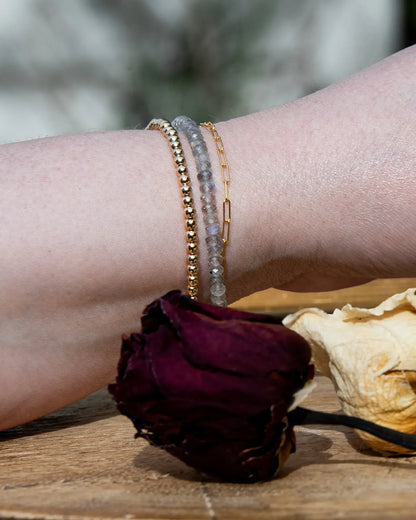 Grey with blue flash Labradorite faceted beaded bracelet stacked on wrist with 14k gold-filled beaded bracelet and 14k gold-filled paperclip chain on wood table