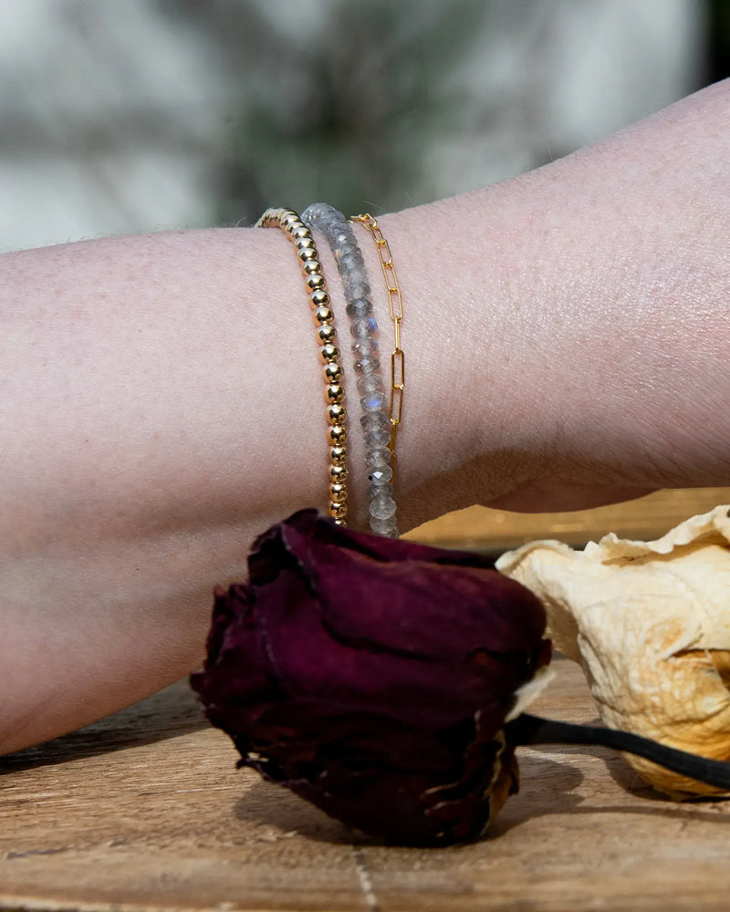 Grey with blue flash Labradorite faceted beaded bracelet stacked on wrist with 14k gold-filled beaded bracelet and 14k gold-filled paperclip chain on wood table