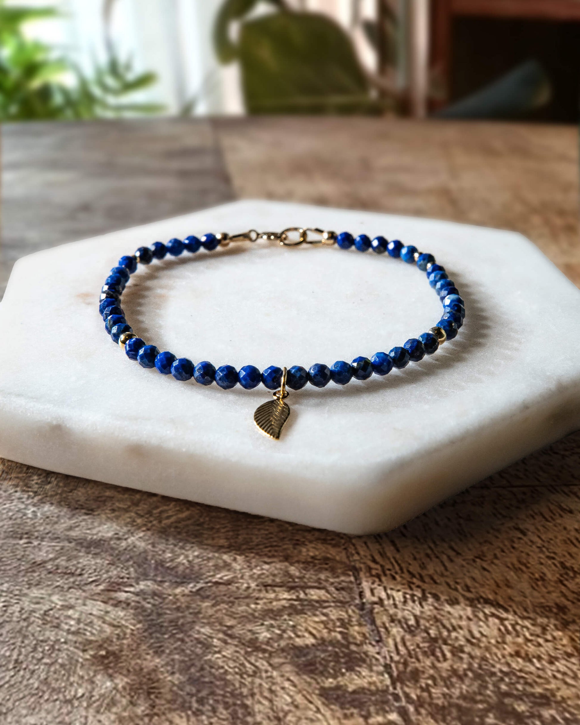 Deep blue lapis lazuli gemstone beaded bracelet with 14k gold-filled leaf-shaped charm and spring ring clasp.