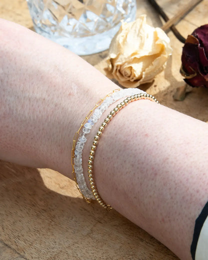 Clear white Moonstone faceted beaded bracelet with flashes of blue stacked on wrist with with 14k gold-filled beaded bracelet and 14k gold-filled paperclip chain on wood table