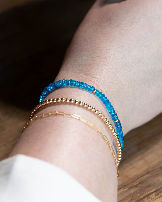 Neon blue Apatite beaded gemstone bracelet with 14k gold-filled accents stacked on a wrist with 14k gold-filled paperclip chain and beaded bracelets.