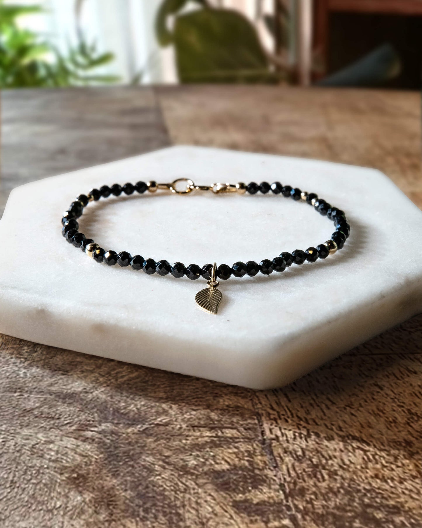 Black onyx gemstone beaded bracelet with 14k gold-filled leaf-shaped charm and spring ring closure.