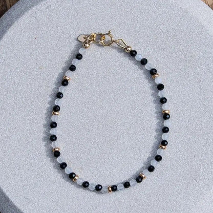 Handcrafted dainty black onyx and white moonstone beaded gemstone bracelet with 14k gold-filled beads, small heart charm, and spring ring clasp. 