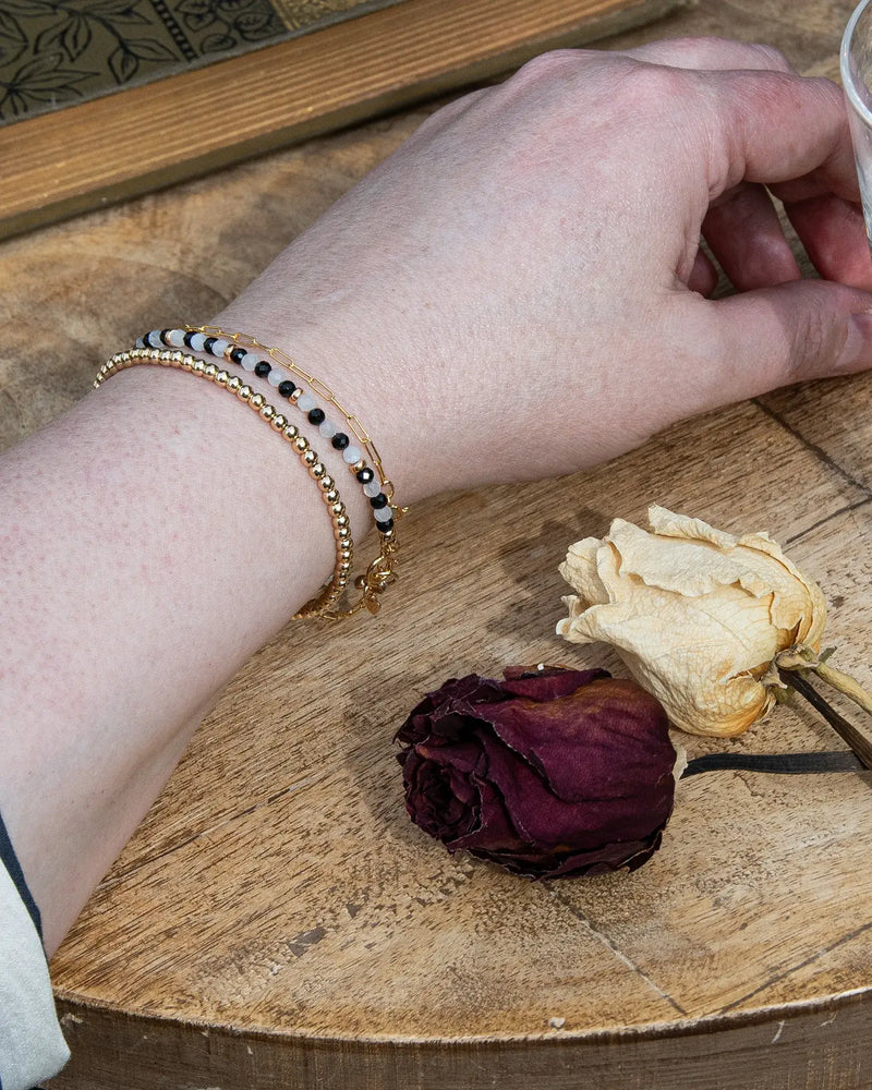 Handcrafted dainty black onyx and white moonstone beaded gemstone bracelet with 14k gold-filled beads, small heart charm, and spring ring clasp. 