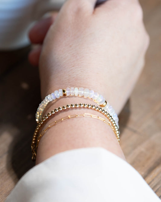 Natural opal gemstone beaded bracelet with rainbow flashes, 14k gold-filled accent beads, and a 14k gold-filled fish-hook clasp stacked on a wrist with 14k gold-filled bracelets.