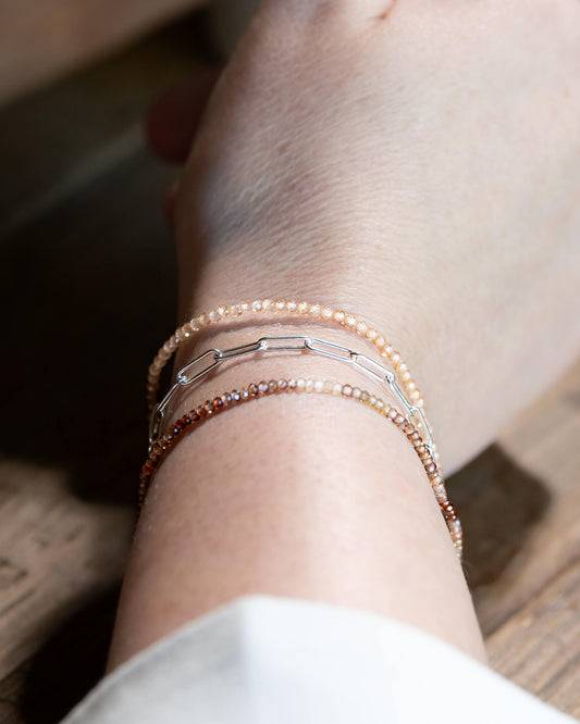 Dainty peach zircon beaded gemstone bracelet stacked on a wrist with brown zircon and sterling silver paperclip chain bracelets.