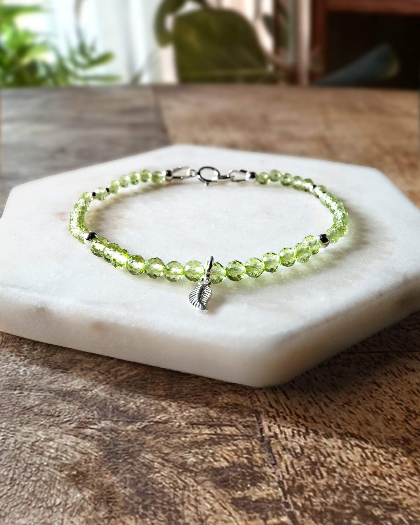 Green peridot gemstone beaded bracelet with sterling silver leaf-shaped charm and spring ring closure.