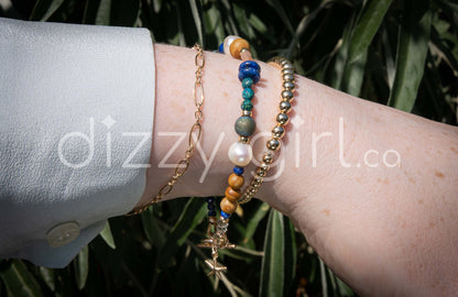 A beaded bracelet with assorted shapes and sizes of Lapis Lazuli, Button Pearl, Wood Jasper, Sunstone, Turquoise, Druzy Quartz, Apetite, and Preciosa Crystal, separated by 14k gold-filled accents beads stacked on a wrist with a 14k gold-filled beaded bracelet and 14k gold-filled chain.