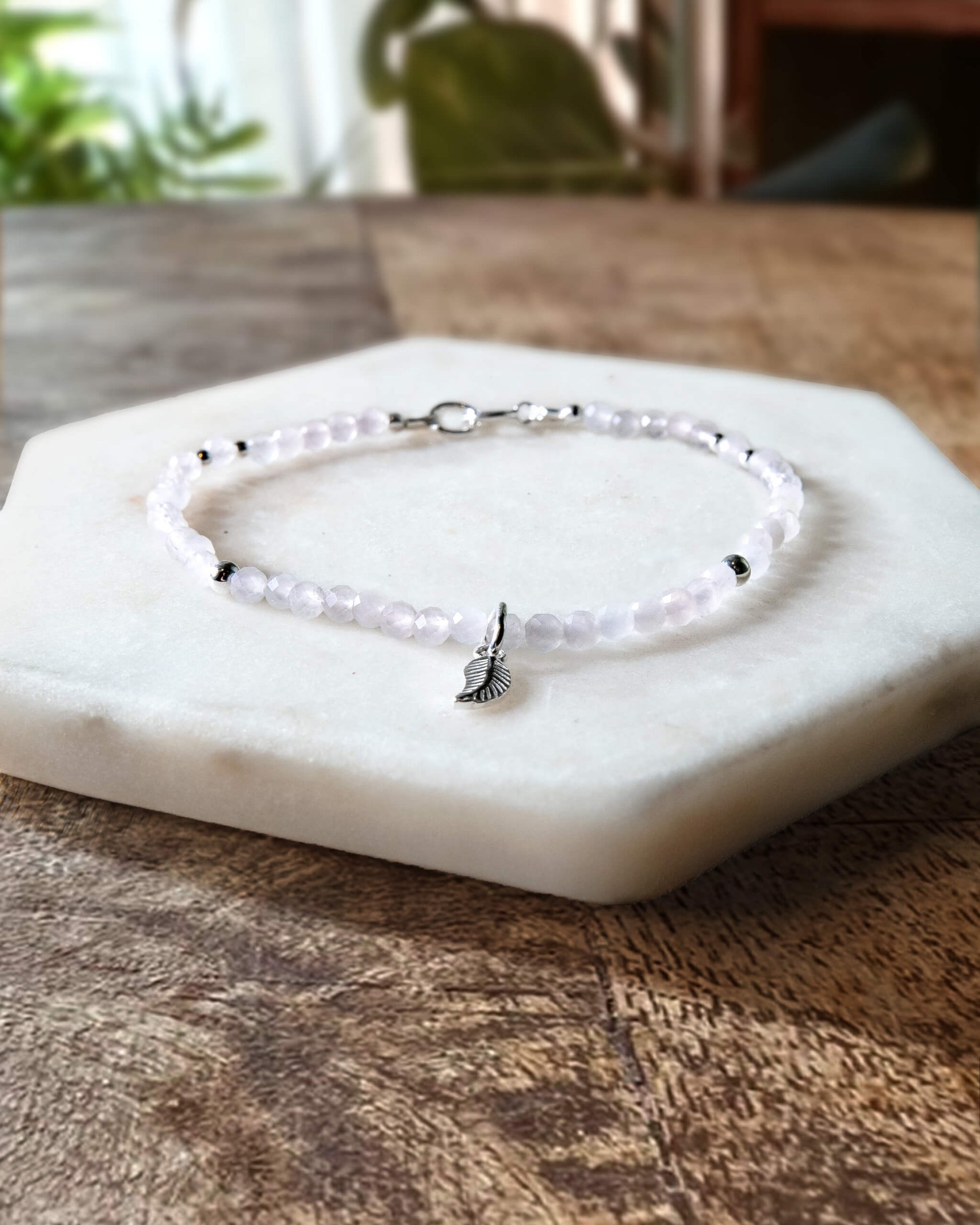 Pale pink rose quartz gemstone beaded bracelet with sterling silver leaf-shaped charm and spring ring closure.