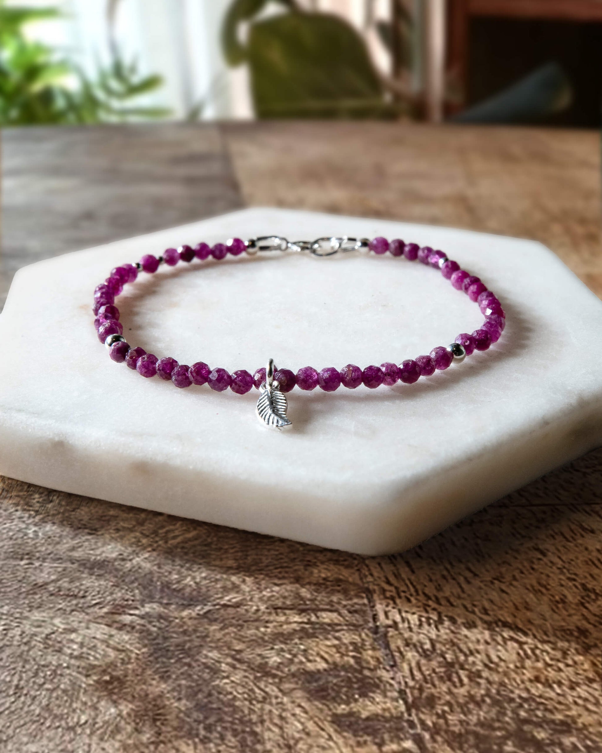 Deep pink ruby gemstone beaded bracelet with sterling silver leaf-shaped charm and spring ring closure.