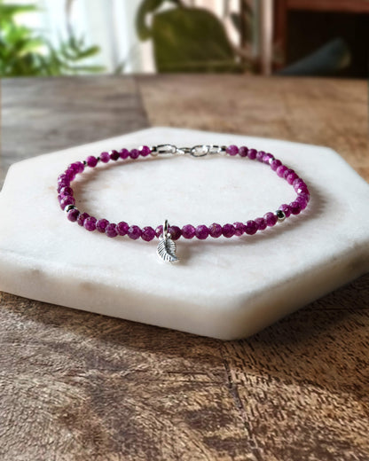 Deep pink ruby gemstone beaded bracelet with sterling silver leaf-shaped charm and spring ring closure.