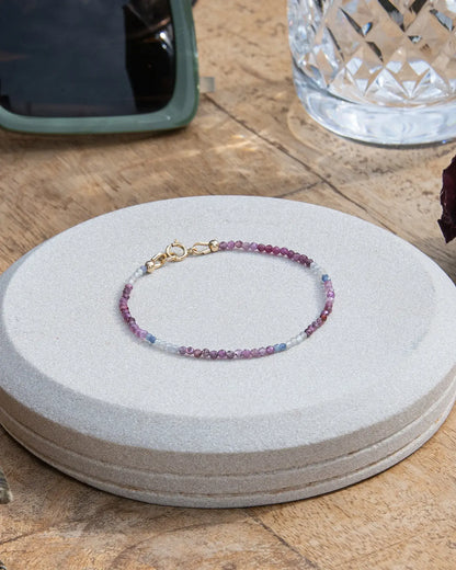 Dainty pink, blue, and white ruby sapphire beaded bracelet with 14k gold-fill spring ring clasp on wooden table