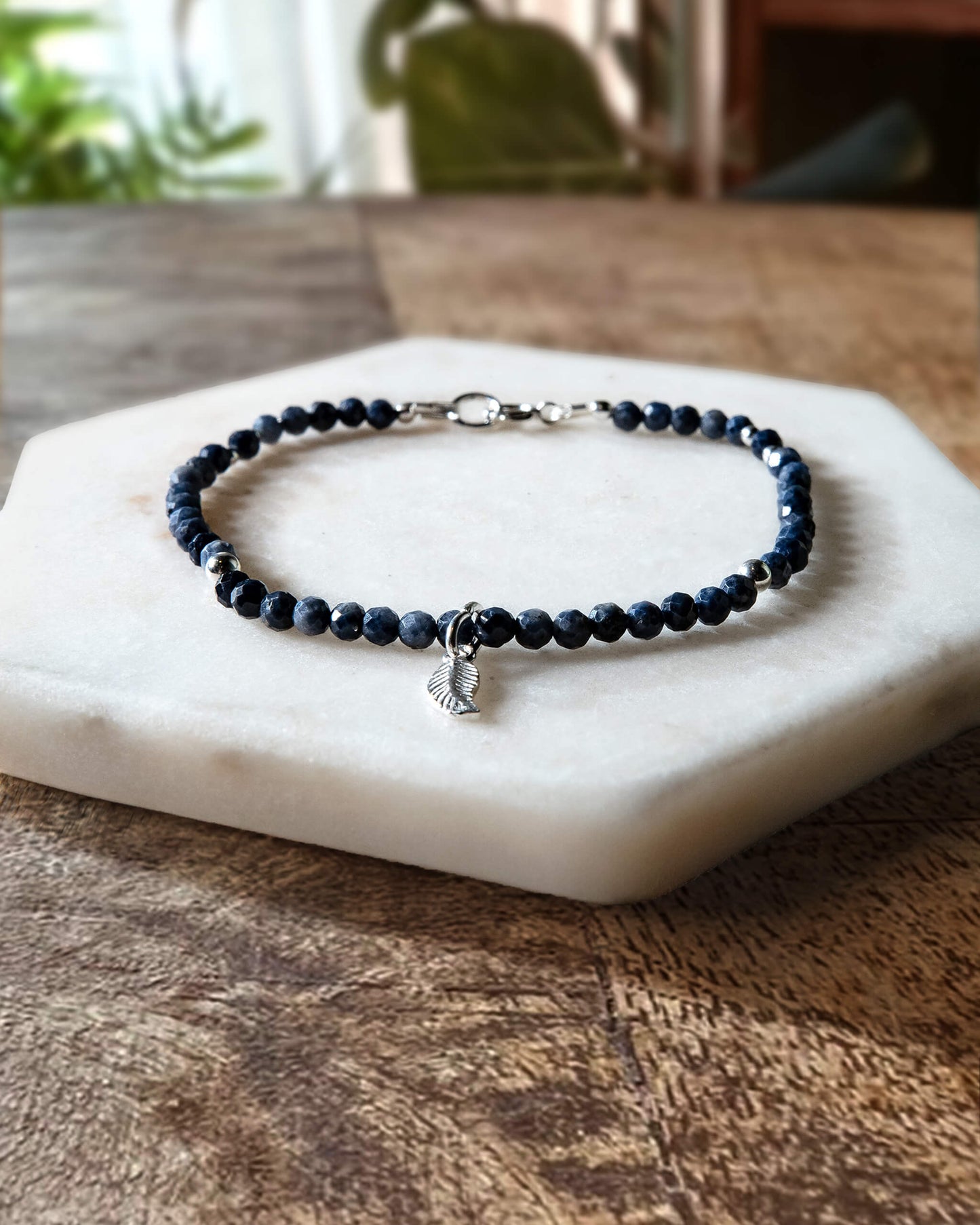 Deep blue sapphire gemstone beaded bracelet with sterling silver leaf-shaped charm and spring ring closure.