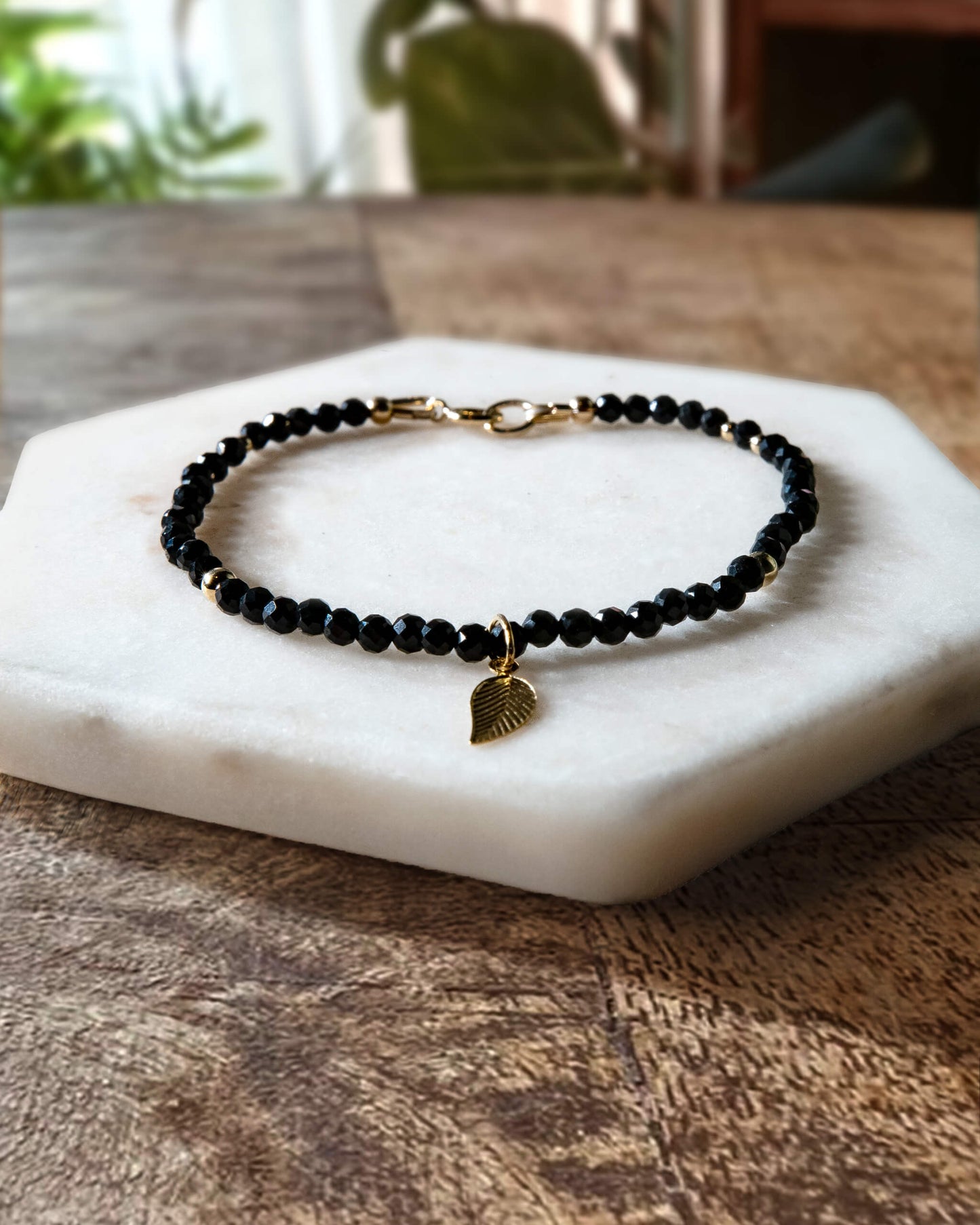 Black spinel gemstone beaded bracelet with 14k gold-filled leaf-shaped charm and spring ring clasp.