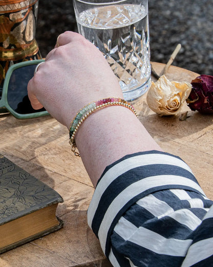 Pink, blue, green, yellow, and brown faceted tourmaline bracelet stacked on wrist with 14k gold-filled beaded bracelet on wood table