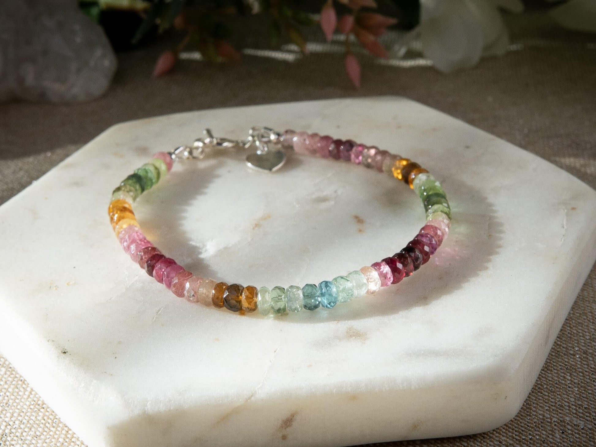 Pink, blue, green, yellow, and brown faceted tourmaline bracelet with sterling silver heart-shaped charm and toggle clasp on white background