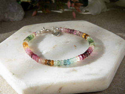 Pink, blue, green, yellow, and brown faceted tourmaline bracelet with sterling silver heart-shaped charm and toggle clasp on white background