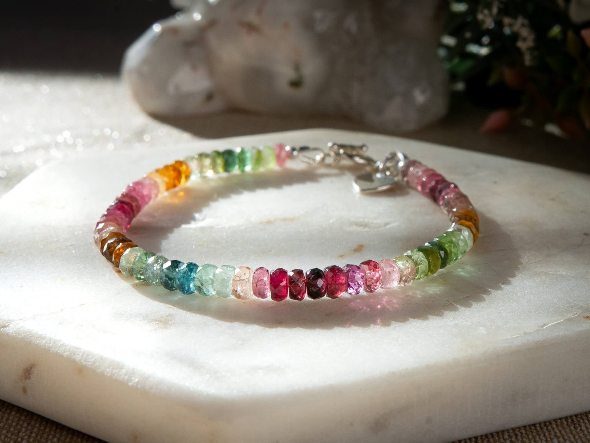 Pink, blue, green, yellow, and brown faceted tourmaline bracelet with sterling silver heart-shaped charm and toggle clasp on white background