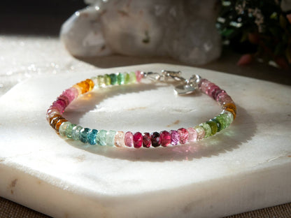 Pink, blue, green, yellow, and brown faceted tourmaline bracelet with sterling silver heart-shaped charm and toggle clasp on white background
